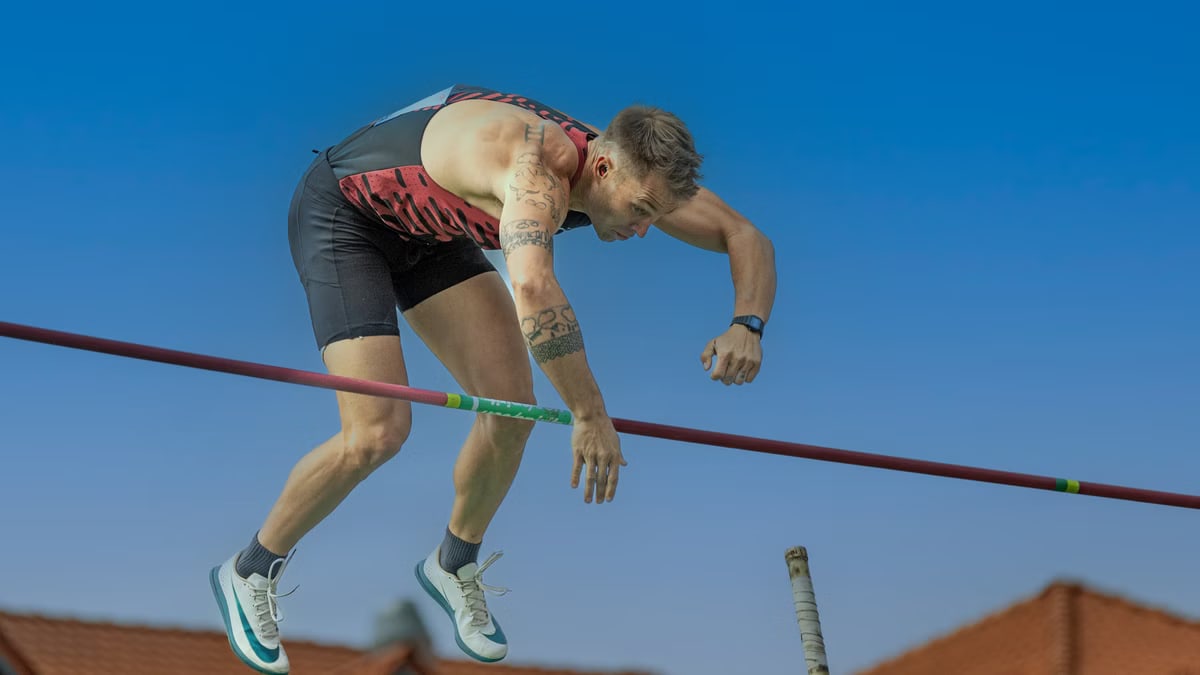 A determined athlete executes a pole vault under a clear blue sky, showcasing strength and focus.